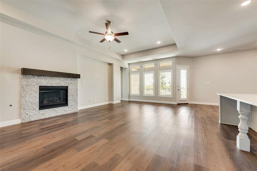 Unfurnished living room with a stone fireplace, ceiling fan, and dark wood-type flooring