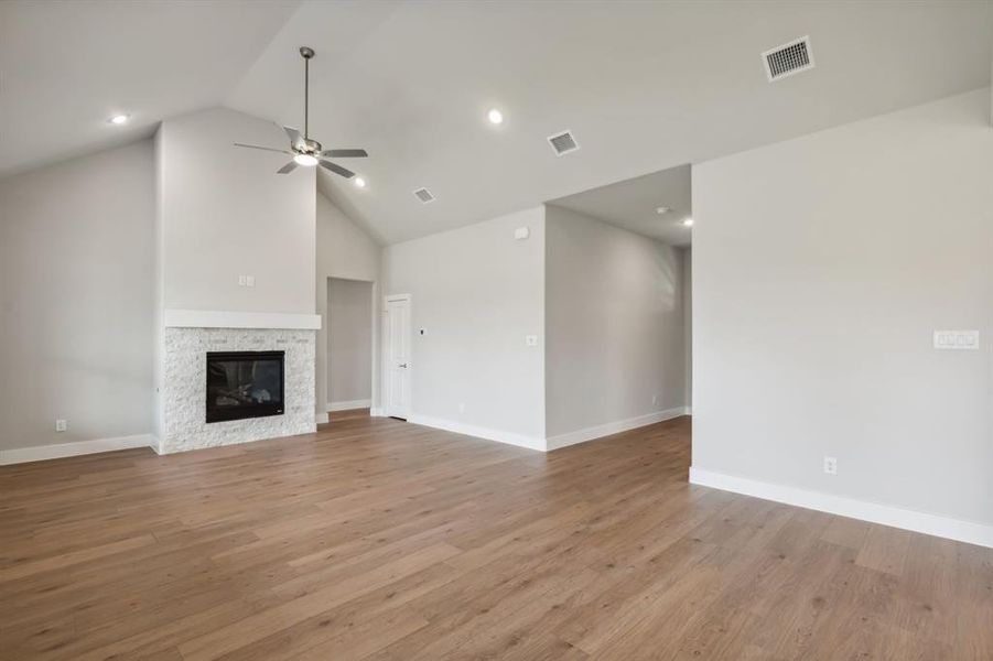 Unfurnished living room featuring ceiling fan, a stone fireplace, light wood-type flooring, and vaulted ceiling