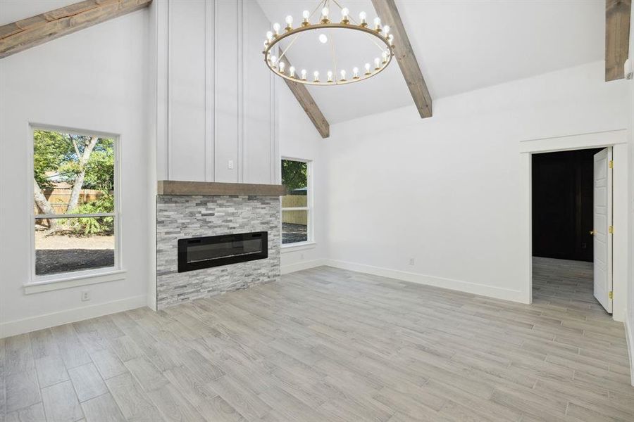 Unfurnished living room with a stone fireplace, high vaulted ceiling, a chandelier, beamed ceiling, and light hardwood / wood-style floors