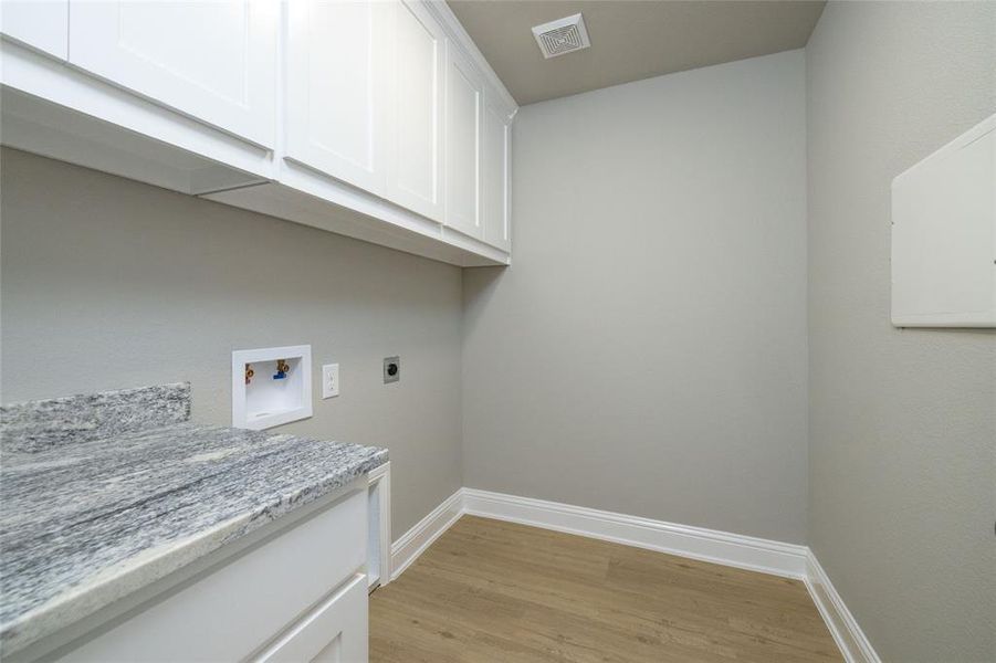 Laundry area with electric dryer hookup, cabinets, washer hookup, and light hardwood / wood-style floors