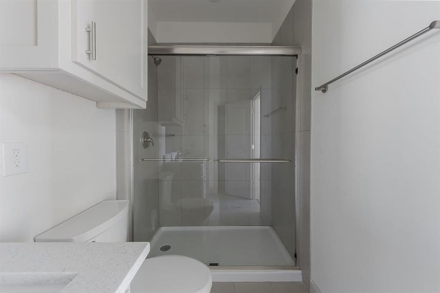 Bathroom featuring tile patterned floors, walk in shower, vanity, and toilet