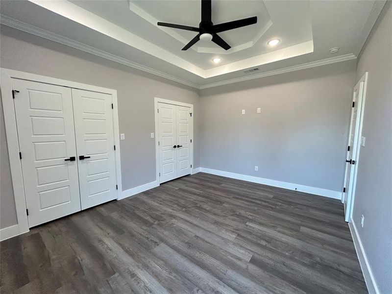 Unfurnished bedroom with ceiling fan, crown molding, a tray ceiling, and dark hardwood / wood-style flooring