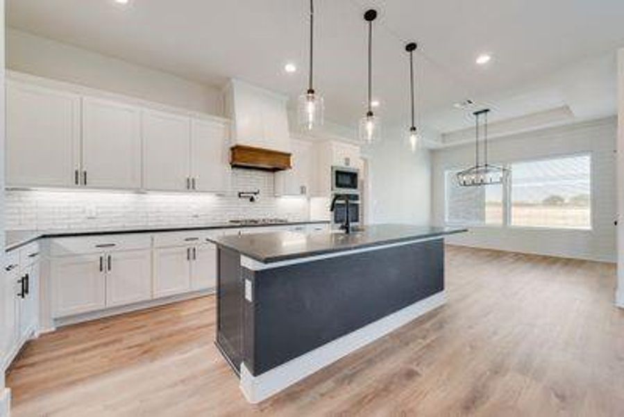 Kitchen featuring white cabinetry, light hardwood / wood-style floors, pendant lighting, premium range hood, and a kitchen island with sink