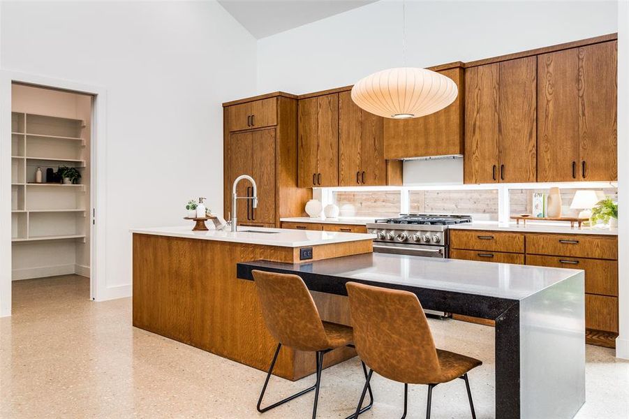 Kitchen featuring stainless steel range, a center island with sink, decorative backsplash, a towering ceiling