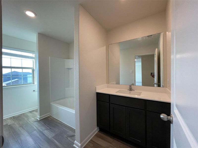 Bathroom with vanity with extensive cabinet space, hardwood / wood-style flooring, and tub / shower combination