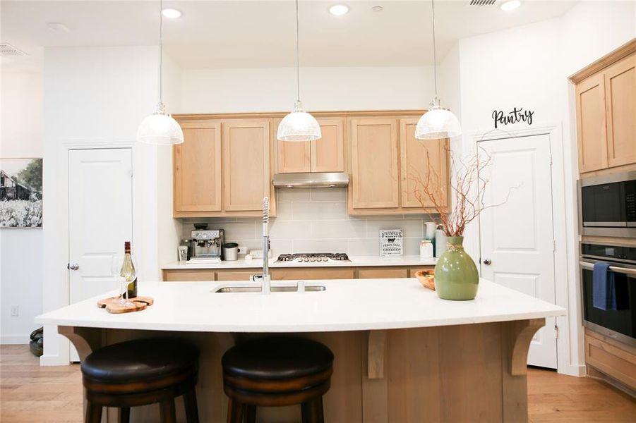 Kitchen with appliances with stainless steel finishes, light hardwood / wood-style flooring, light brown cabinets, decorative backsplash, and an island with sink