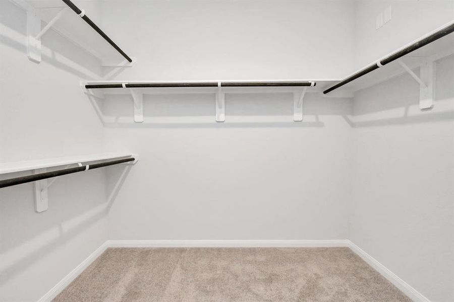 Enjoy this spacious walk-in closet with high ceilings, a plush carpet and bright recessed lights.