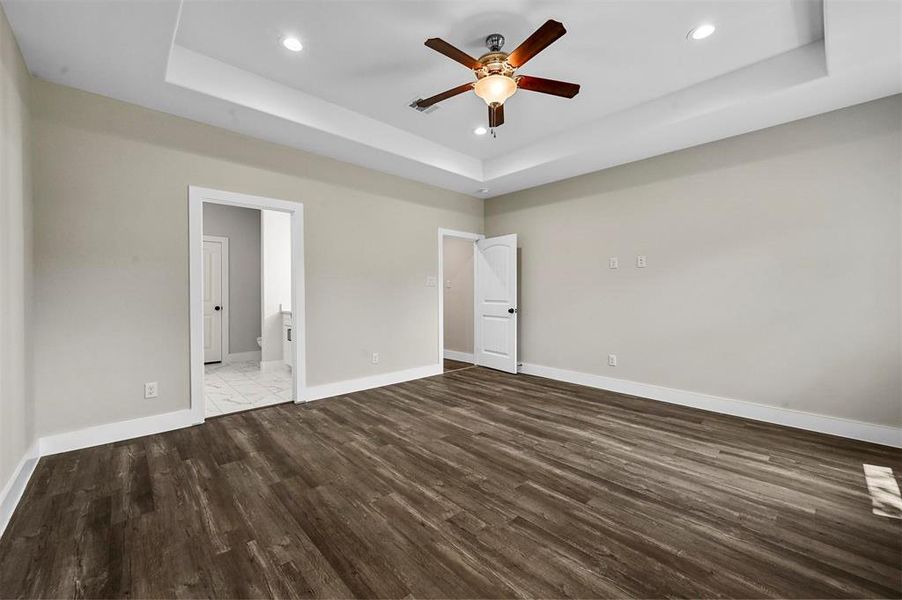 Unfurnished bedroom featuring ensuite bath, ceiling fan, dark tile patterned flooring, and a tray ceiling