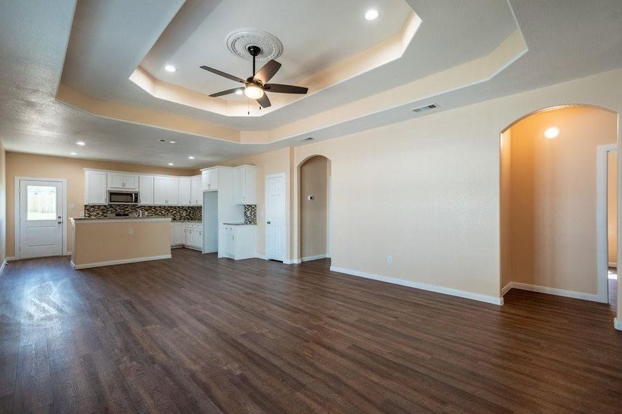 Unfurnished living room featuring dark hardwood / wood-style flooring, ceiling fan, and a raised ceiling