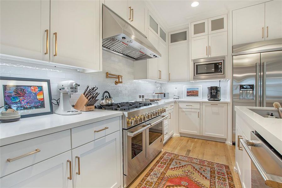 Kitchen with built in appliances, backsplash, white cabinetry, and light wood-type flooring
