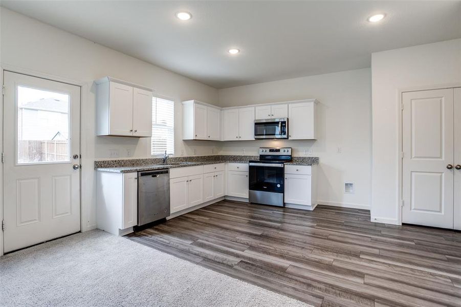 Kitchen with white cabinets, light stone counters, stainless steel appliances, dark carpet, and sink