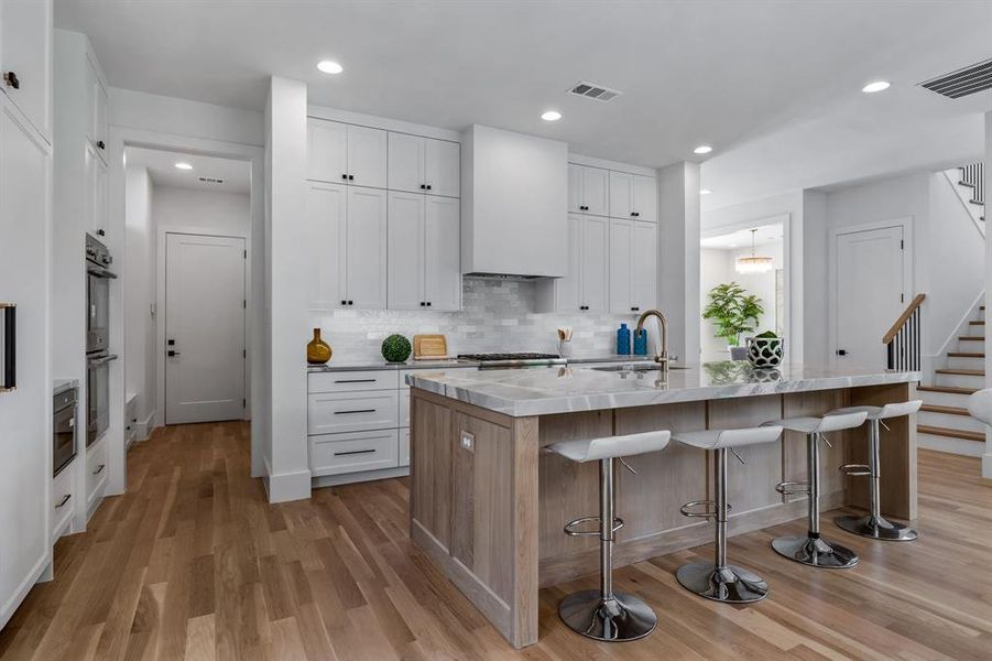 Kitchen featuring white cabinetry, tasteful backsplash, light wood-type flooring, sink, and a center island with sink