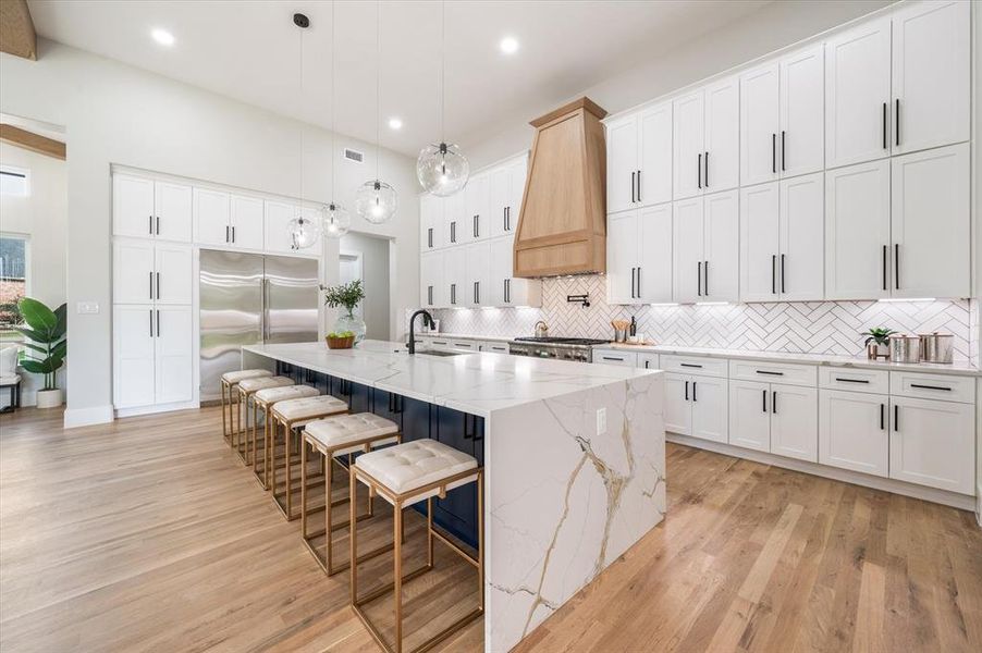 Kitchen featuring custom range hood, white cabinets, and a large island