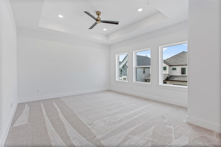 Unfurnished room featuring ceiling fan, a raised ceiling, and light colored carpet
