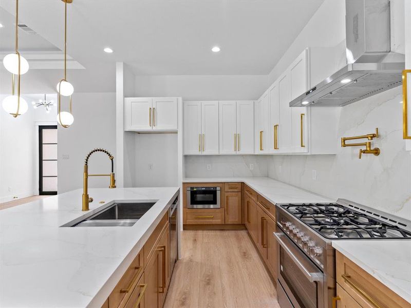 Kitchen with white cabinetry, stainless steel appliances, decorative light fixtures, sink, and wall chimney range hood