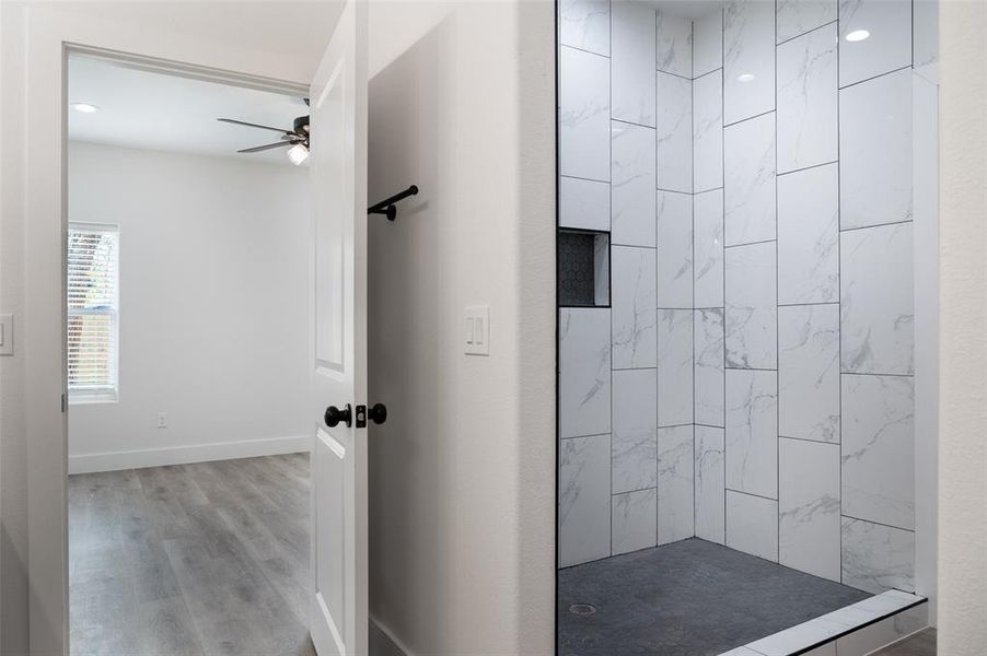 Bathroom with tiled shower, wood-type flooring, and ceiling fan