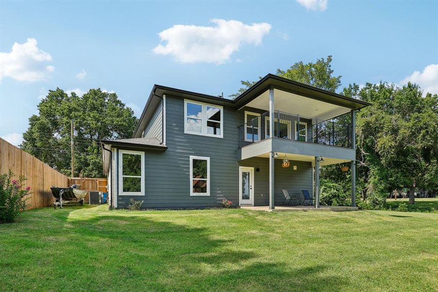 Rear view of property featuring a balcony, central AC unit, and a yard