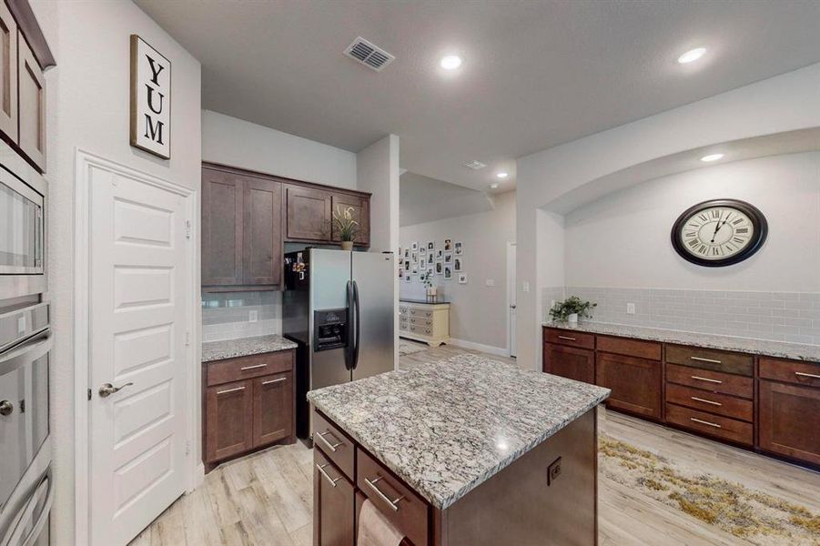 Kitchen featuring tasteful backsplash, light wood-type flooring, a center island, light stone counters, and stainless steel appliances