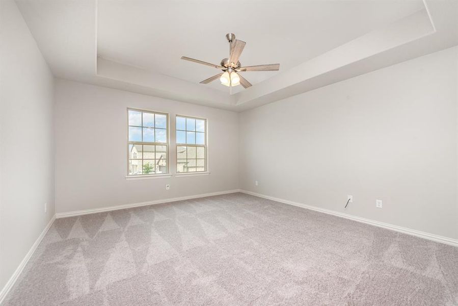 Spare room featuring carpet flooring, ceiling fan, and a tray ceiling