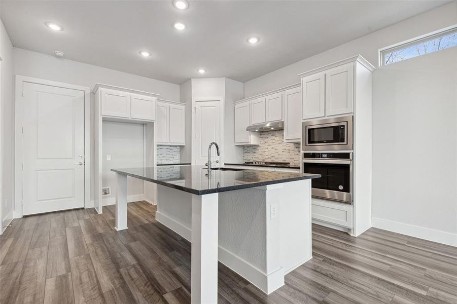 Kitchen with appliances with stainless steel finishes, white cabinetry, backsplash, and hardwood / wood-style floors