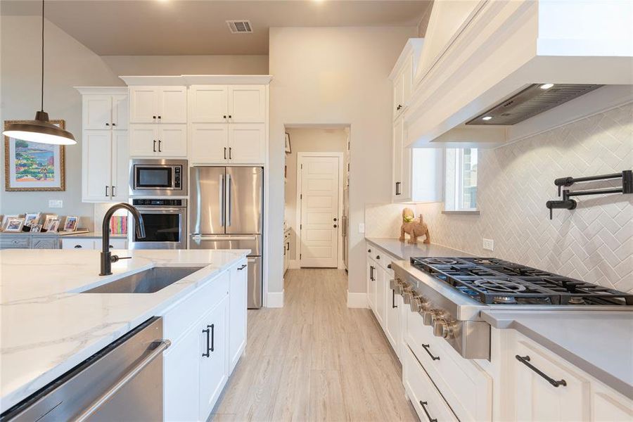 Kitchen featuring sink, white cabinets, custom exhaust hood, appliances with stainless steel finishes, and decorative light fixtures