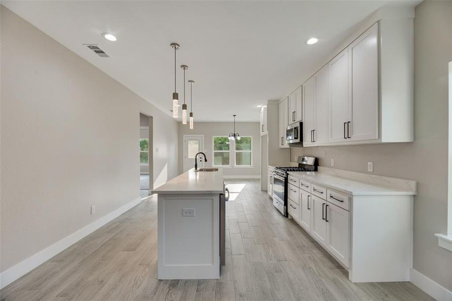 Kitchen featuring white cabinetry, pendant lighting, sink, a center island with sink, and appliances with stainless steel finishes