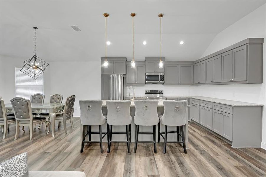 Kitchen with stainless steel appliances, gray cabinets, hanging light fixtures, and lofted ceiling