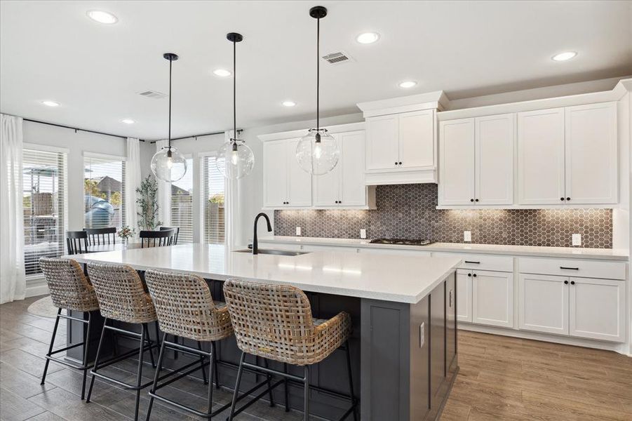 This is a modern, open-concept kitchen with white cabinetry, stainless steel appliances, a large island with bar seating, and pendant lighting. It overlooks a casual eating area with a view of the backyard.