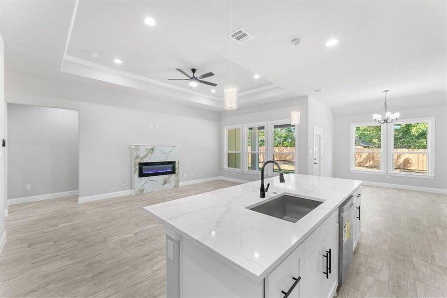 Kitchen with hanging light fixtures, light stone counters, white cabinets, a center island with sink, and sink