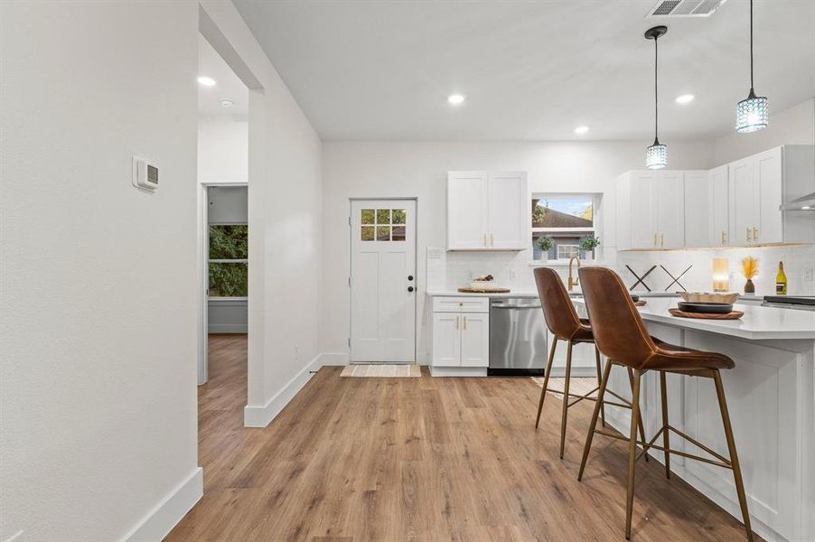 Kitchen with stainless steel dishwasher, white cabinets, light wood-type flooring, and a healthy amount of sunlight