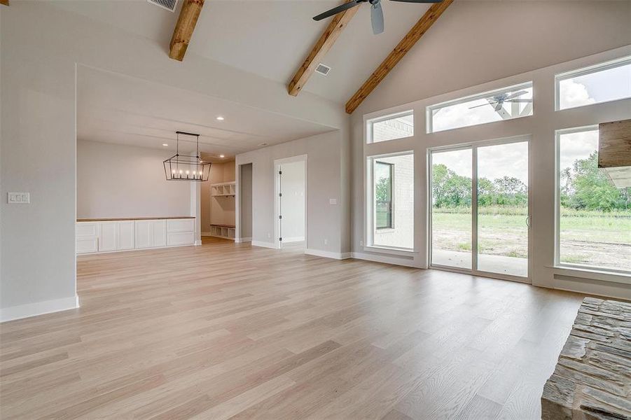 Unfurnished living room with beamed ceiling, light hardwood / wood-style floors, plenty of natural light, and ceiling fan with notable chandelier