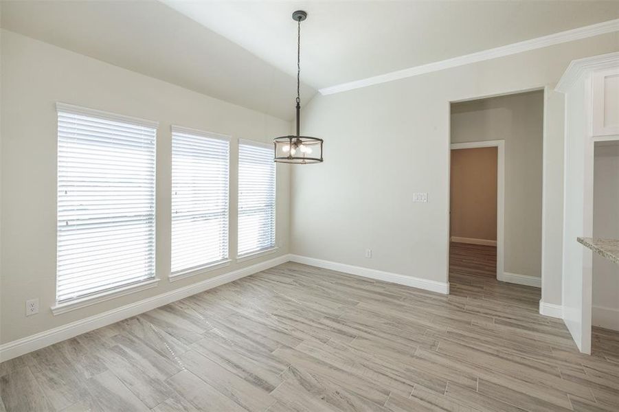 Unfurnished dining area with light hardwood / wood-style floors, crown molding, and a notable chandelier