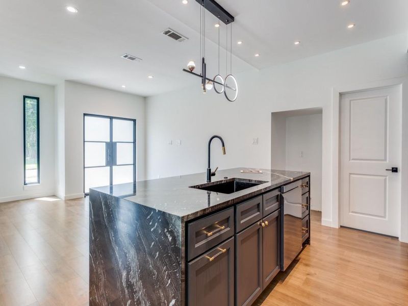 Kitchen with dark stone counters, light hardwood / wood-style floors, sink, hanging light fixtures, and a center island with sink