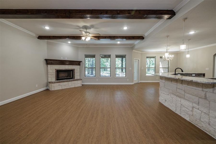 Unfurnished living room featuring ornamental molding, beamed ceiling, a fireplace, and dark wood-type flooring