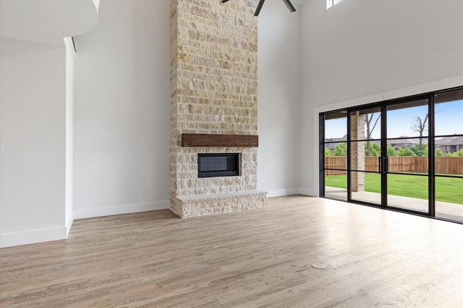 Unfurnished living room with a towering ceiling, light wood-type flooring, and a fireplace