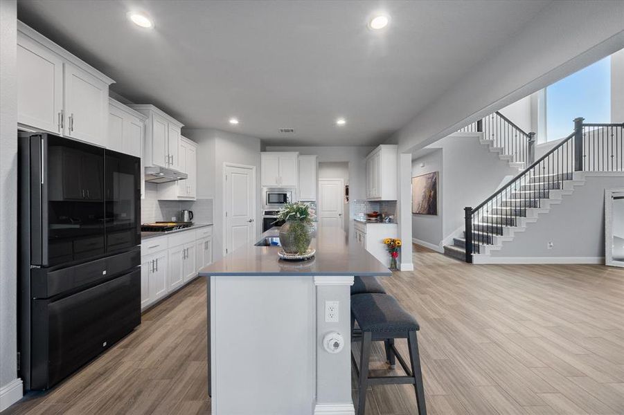 Kitchen featuring white cabinets, an island with sink, stainless steel appliances, and a kitchen bar