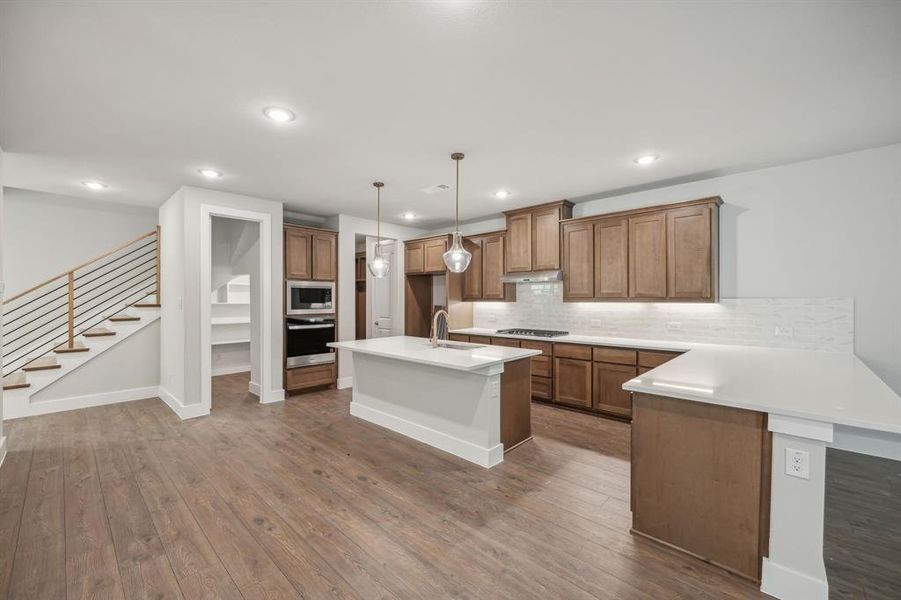 Kitchen with warm wood-type flooring, stainless steel appliances, pendant lighting, and a center island with sink