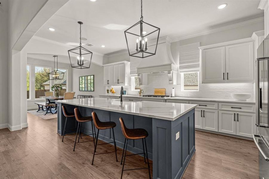 Kitchen with a kitchen island with sink, decorative light fixtures, light wood-type flooring, and white cabinetry