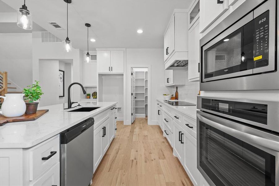 Kitchen featuring light hardwood / wood-style flooring, decorative light fixtures, appliances with stainless steel finishes, white cabinetry, and sink