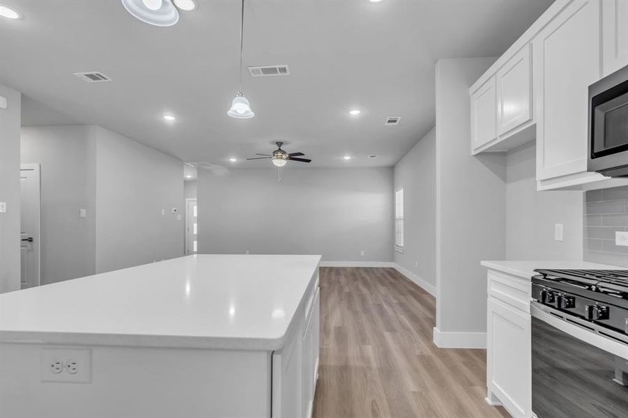 Kitchen featuring appliances with stainless steel finishes, decorative light fixtures, a center island, and white cabinets