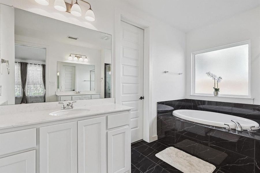 Bathroom featuring tiled tub and vanity