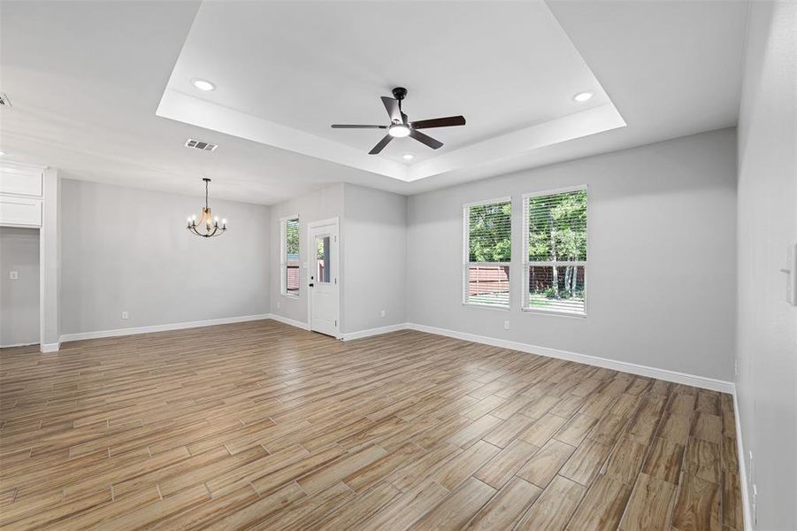 Unfurnished room featuring light hardwood / wood-style flooring, ceiling fan with notable chandelier, and a tray ceiling