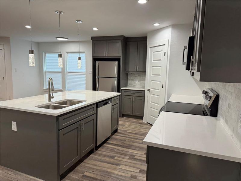 Kitchen with a center island with sink, pendant lighting, appliances with stainless steel finishes, dark wood-type flooring, and sink