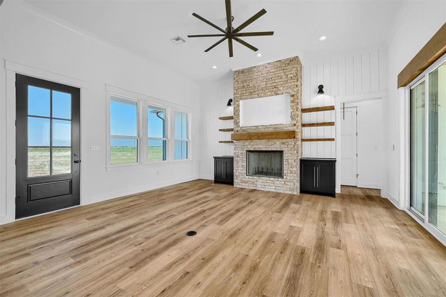 Unfurnished living room with brick wall, light hardwood / wood-style flooring, a fireplace, and ceiling fan