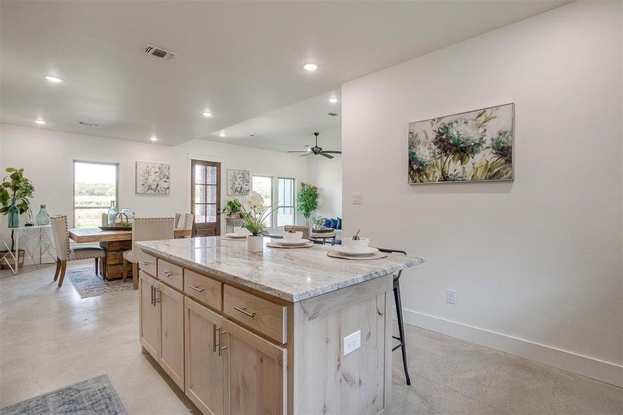 Kitchen featuring a kitchen island, a breakfast bar area, light stone countertops, light brown cabinetry, and ceiling fan