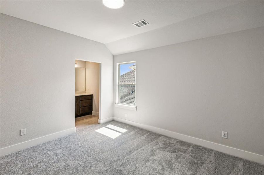 Unfurnished bedroom with light colored carpet, ensuite bath, and vaulted ceiling