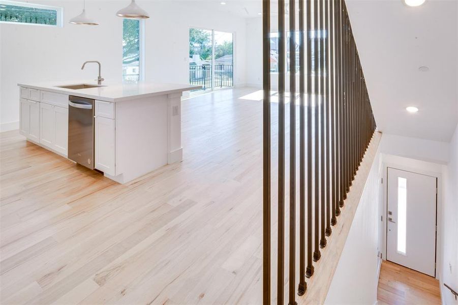 Kitchen with sink, pendant lighting, light wood-type flooring, stainless steel dishwasher, and white cabinets