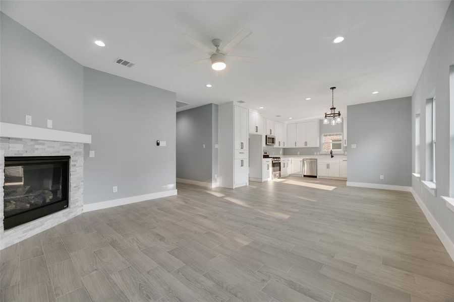 Unfurnished living room featuring a stone fireplace, sink, ceiling fan, and light hardwood / wood-style floors