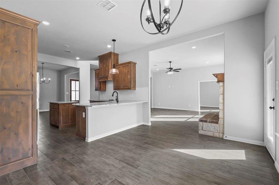 Kitchen featuring hanging light fixtures, ceiling fan with notable chandelier, dark hardwood / wood-style floors, kitchen peninsula, and a stone fireplace