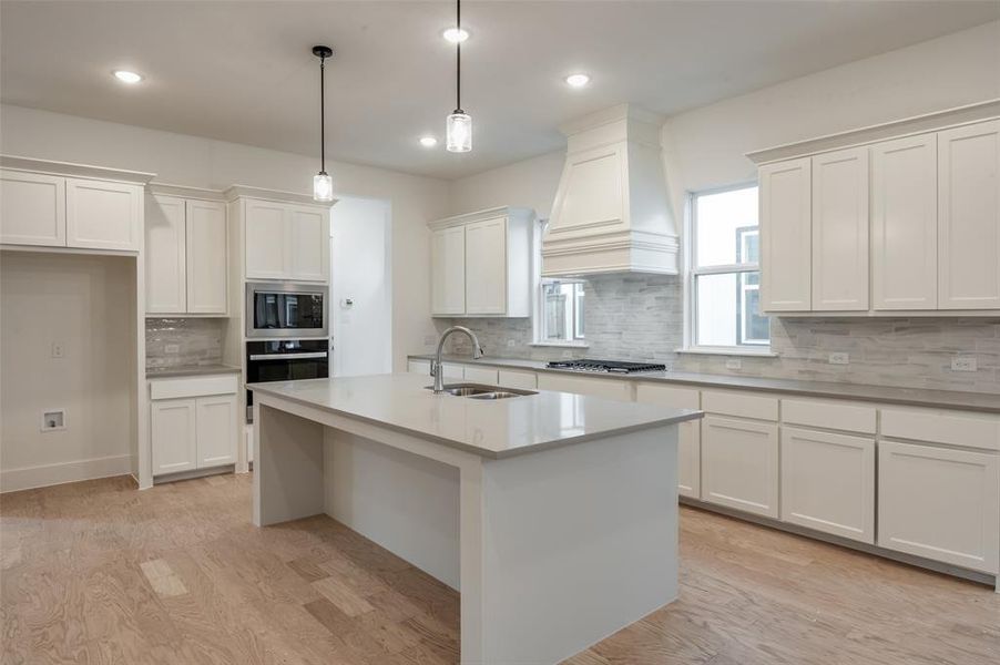 Kitchen featuring light wood-type flooring, sink, custom range hood, and stainless steel appliances